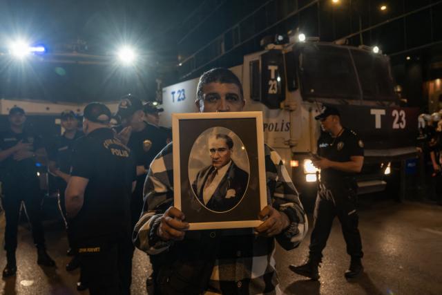 A man holds a portrait of Mustafa Kemal Ataturk, founder of modern Turkey, in front of a police water cannon as protesters chant slogans during a demonstration against Izmir mayor Cemil Tugay's defection to the ruling AKP party, in Izmir on October 7, 2026. More than 1,000 protesters gathered in Turkish opposition stronghold Izmir on October 7, 2026, angered by the defection of the city's mayor to President Recep Tayyip Erdogan's ruling AKP. The move was a huge symbolic victory for the Turkish leader, who has long wanted to control the secular resort city of 4.5 million people on Turkey's Aegean coast which has been held by the opposition for nearly 30 years. (Photo by Murat Kocabas / AFP)