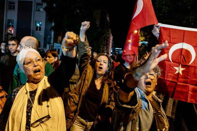 A protester holds a Turkish national flag while others chant slogans during a demonstration against Izmir mayor Cemil Tugay's defection to the ruling AKP party, in Izmir on October 7, 2026. More than 1,000 protesters gathered in Turkish opposition stronghold Izmir on October 7, 2026, angered by the defection of the city's mayor to President Recep Tayyip Erdogan's ruling AKP. The move was a huge symbolic victory for the Turkish leader, who has long wanted to control the secular resort city of 4.5 million people on Turkey's Aegean coast which has been held by the opposition for nearly 30 years. (Photo by Murat Kocabas / AFP)