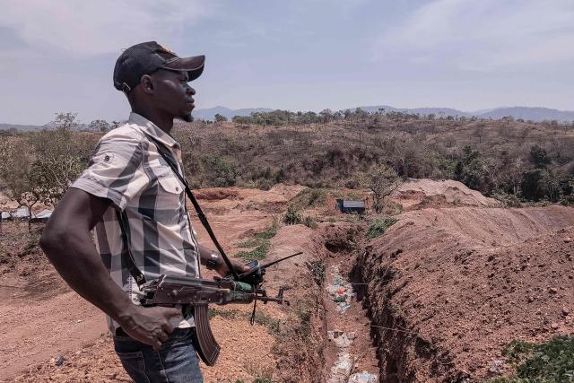 An armed local militia fighter stands in front of an artisanal gold mine in Mwala, Democratic Republic of the Congo's Tanganyika province, on September 25, 2026. A handful of teenagers, Kalashnikovs in hand, guard a gold mine in southeastern Democratic Republic of Congo, where local militias are milking guns and profits from the government's ongoing conflict with the M23 armed group. In Mwala, a small mining village in Tanganyika, around a hundred heavily armed militiamen, most of them originally from South Kivu, rule the roost. (Photo by Camille Laffont / AFP)
