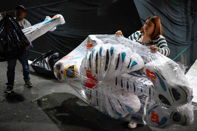 Two store employees hold skulls made using a traditional papier-mache technique at the Jamaica Market in Mexico City on October 7, 2026. (Photo by Alfredo ESTRELLA / AFP)