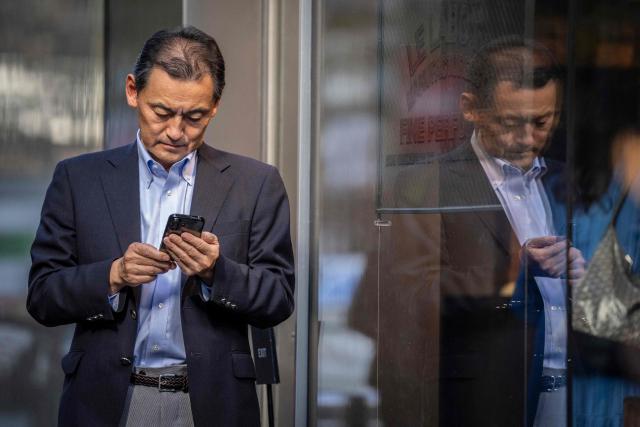 A man checks his phone on a street in Tokyo on October 8, 2026. (Photo by Yuichi YAMAZAKI / AFP)