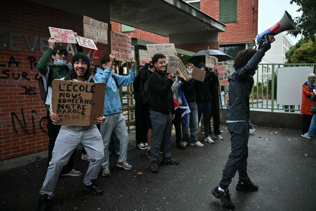 A high-school student protester chant slogans in a loudspeaker among protesters holding placards during a blockade of high-school Deodat de Severac in Toulouse, on October 8, 2026, as part of a nationwide protest movement over learning conditions. Since late September, pupils have barred the entrances to hundreds of schools, complaining of teacher absences, overloaded timetables, dilapidated classrooms and buildings ill-adapted to rising temperatures, among other grievances. (Photo by Lionel BONAVENTURE / AFP)