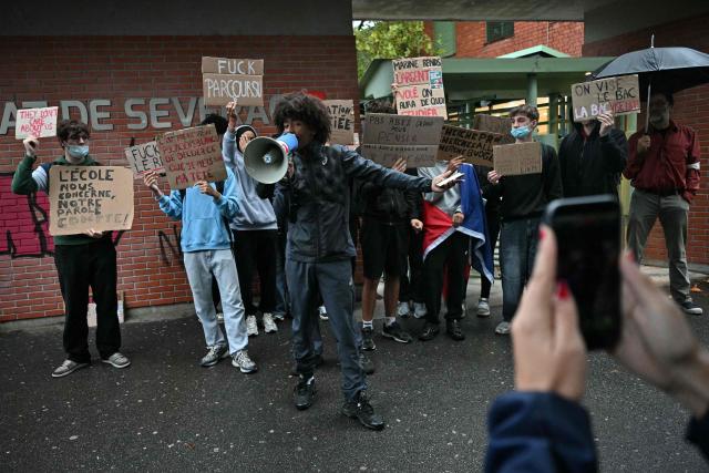 A high-school student protester chant slogans in a loudspeaker among protesters holding placards during a blockade of high-school Deodat de Severac in Toulouse, on October 8, 2026, as part of a nationwide protest movement over learning conditions. Since late September, pupils have barred the entrances to hundreds of schools, complaining of teacher absences, overloaded timetables, dilapidated classrooms and buildings ill-adapted to rising temperatures, among other grievances. (Photo by Lionel BONAVENTURE / AFP)