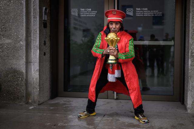 Moroccan supporter Noureddine Falah, aka “Dolmy” poses with a replica Africa Cup of Nations trophy in front of the Court of Arbitration for Sport (CAS) during a hearing on Senegal’s appeal against Morocco following a chaotic Africa Cup of Nations football final, in Lausanne on October 8, 2026. Nearly ten months after a chaotic Africa Cup of Nations final, the dispute is set to reach its conclusion in Lausanne, where the Court of Arbitration for Sport (CAS) will hear Senegal’s appeal against Morocco being awarded the title. Senegal had initially won the January 18 final 1-0 after extra time, in a match marred by a lengthy walk-off over a controversial late penalty. (Photo by Fabrice COFFRINI / AFP)