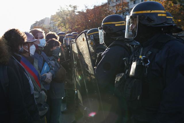 Adult protesters (L) form a chain with their arms to protect teenagers on a blockade action next to French Republican Security Corps (CRS - Compagnies Republicaines de Securite) police officers in riot gear (R) near Helene Boucher high-school during a demonstration of high-school students in Paris, on October 8, 2026, as part of a nationwide protest movement over learning conditions. Since late September, pupils have barred the entrances to hundreds of schools, complaining of teacher absences, overloaded timetables, dilapidated classrooms and buildings ill-adapted to rising temperatures, among other grievances. (Photo by SIMON WOHLFAHRT / AFP)