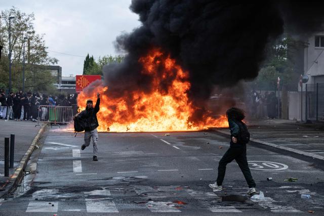 A protester runs in front of trash cans burning during a blockade of high-school Toulouse-Lautrec in Toulouse, on October 8, 2026, as part of a nationwide protest movement over learning conditions. Since late September, pupils have barred the entrances to hundreds of schools, complaining of teacher absences, overloaded timetables, dilapidated classrooms and buildings ill-adapted to rising temperatures, among other grievances. (Photo by Lionel BONAVENTURE / AFP)