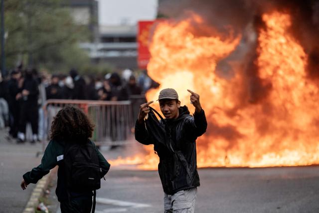 A protester gives a middle finger as trash cans burn during a blockade of high-school Toulouse-Lautrec in Toulouse, on October 8, 2026, as part of a nationwide protest movement over learning conditions. Since late September, pupils have barred the entrances to hundreds of schools, complaining of teacher absences, overloaded timetables, dilapidated classrooms and buildings ill-adapted to rising temperatures, among other grievances. (Photo by Lionel BONAVENTURE / AFP)