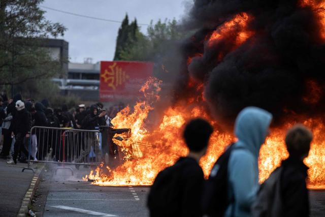 Protesters gather as trash cans burn during a blockade of high-school Toulouse-Lautrec in Toulouse, on October 8, 2026, as part of a nationwide protest movement over learning conditions. Since late September, pupils have barred the entrances to hundreds of schools, complaining of teacher absences, overloaded timetables, dilapidated classrooms and buildings ill-adapted to rising temperatures, among other grievances. (Photo by Lionel BONAVENTURE / AFP)