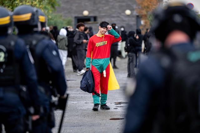A dressed up protester faces riot police during a blockade of high-school Toulouse-Lautrec in Toulouse, on October 8, 2026, as part of a nationwide protest movement over learning conditions. Since late September, pupils have barred the entrances to hundreds of schools, complaining of teacher absences, overloaded timetables, dilapidated classrooms and buildings ill-adapted to rising temperatures, among other grievances. (Photo by Valentine CHAPUIS / AFP)