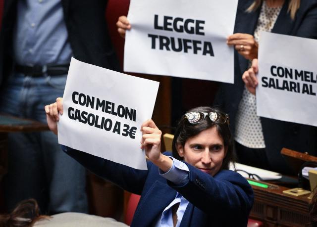 Secretary of the Democratic Party (PD) Elly Schlein holds a sign reading "With Meloni, gasoline at 3 euros" in the Chamber of Deputies, Italy's lower house of parliament, during a session for a vote that will decide on a final approval of a new electoral reform, in Rome on October 8, 2026. Italy's parliament votes on a reform of the country's electoral law that opposition parties say the prime minister's hard-right government has designed to boost its chances of re-election next year. The proposal would introduce a fully proportional system that guarantees a parliamentary majority to any alliance winning more than 42 percent of the vote. (Photo by Tiziana FABI / AFP)
