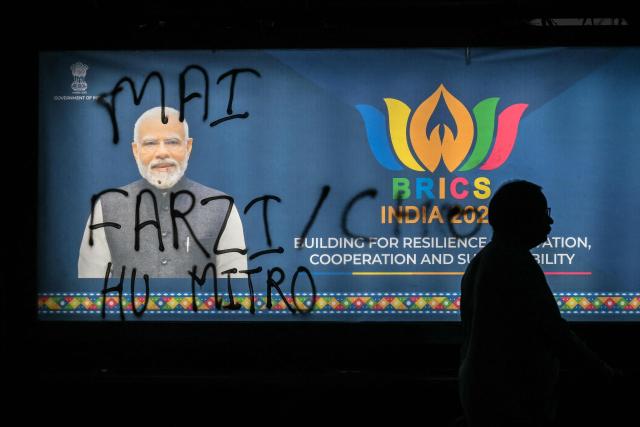 A man walks past a poster of India's Prime Minister Narendra Modi with graffiti on it during an ongoing protest by the opposition alliance INDIA bloc (Indian National Developmental Inclusive Alliance) in New Delhi on October 8, 2026, against the country's Chief Election Commissioner Gyanesh Kumar calling for his resignation over alleged irregularities in the Special Intensive Revision (SIR) of electoral rolls. (Photo by Arun SANKAR / AFP)