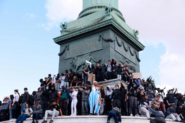 Protesters climb the July Column during a demonstration of high-school students at Place de la Bastille, in Paris, on October 8, 2026, as part of a nationwide protest movement over learning conditions. Since late September, pupils have barred the entrances to hundreds of schools, complaining of teacher absences, overloaded timetables, dilapidated classrooms and buildings ill-adapted to rising temperatures, among other grievances. (Photo by Kenzo TRIBOUILLARD / AFP)