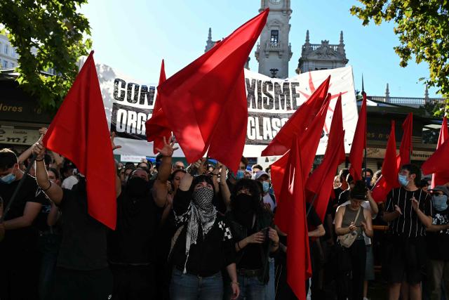 People at a housing rights activists' camp hold red flags ahead of a demonstration called by far-right groups seeking the camp's eviction at City Hall Square in Valencia, eastern Spain, on October 8, 2026. (Photo by JOSE JORDAN / AFP)