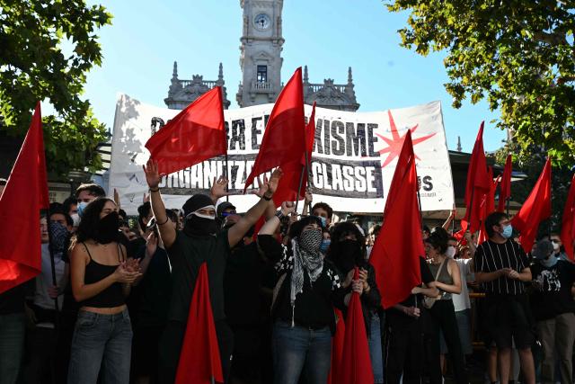 People at a housing rights activists' camp hold red flags ahead of a demonstration called by far-right groups seeking the camp's eviction at City Hall Square in Valencia, eastern Spain, on October 8, 2026. (Photo by JOSE JORDAN / AFP)