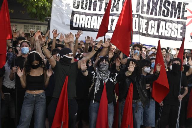 People at a housing rights activists' camp raise their hands and hold red flags ahead of a demonstration called by far-right groups seeking the camp's eviction at City Hall Square in Valencia, eastern Spain, on October 8, 2026. (Photo by Jose JORDAN / AFP)