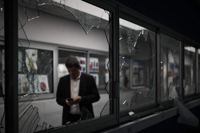 A man stands behind shattered windows in a corridor of the "Les Iris" high school in Lormont near Bordeaux, southwestern France, on October 8, 2026, after youths ransacked part of the school, stealing around ten computers and setting fire to a stockpile of paper, according to the headteacher. Since late September, pupils have barred the entrances to hundreds of schools, complaining of teacher absences, overloaded timetables, dilapidated classrooms and buildings ill-adapted to rising temperatures, among other grievances. (Photo by Philippe LOPEZ / AFP)