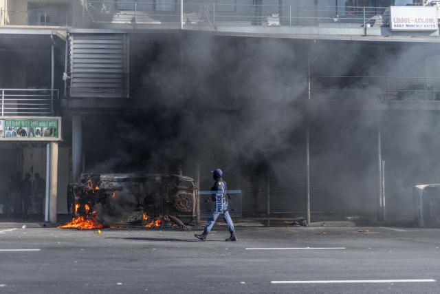 TOPSHOT - A South African Police Service (SAPS) officer intervene to evacuate foreign nationals from a building as clashes erupt between protesters and foreign nationals in Durban on October 8, 2026. Several vehicles were set alight during the confrontation amid tensions over undocumented immigration and foreign nationals. (Photo by RAJESH JANTILAL / AFP)