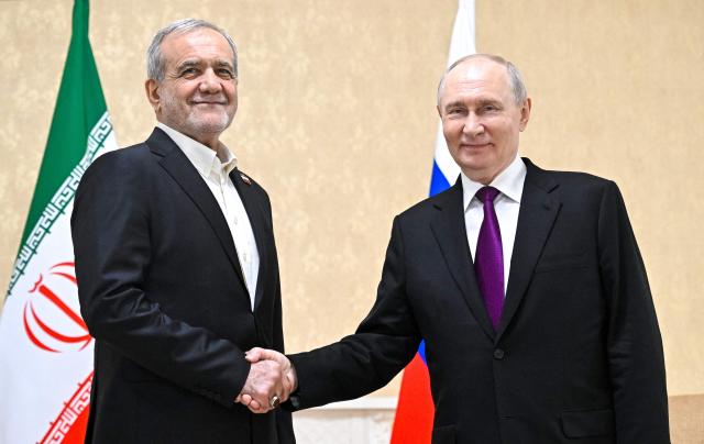 TOPSHOT - In this pool photograph distributed by the Russian state agency Sputnik, Russia's President Vladimir Putin and Iranian President Masoud Pezeshkian shake hands during a meeting in Turkmenbashi on October 8, 2026. (Photo by Sergei BOBYLYOV / POOL / AFP)