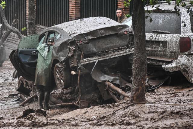 People inspect vehicles damaged and covered in mud following a mudslide in the Las Condes district of Santiago on October 8, 2026. (Photo by RODRIGO ARANGUA / AFP)
