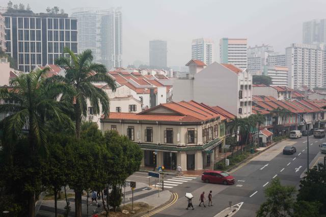 Pedestrians walk across a road as buildings are seen shrouded by haze in Singapore on October 9, 2026. Indonesia has been battling fires for weeks in parts of Borneo and Sumatra, sending suffocating haze across the islands and neighbouring Malaysia and Singapore. (Photo by ANTHONY WALLACE / AFP)