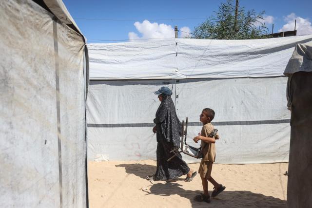 This photo taken on October 6, 2026 shows Nihaya Al-Masri, a 35-year-old displaced Palestinian woman from Beit Hanoun, walking past tents at a makeshift camp where she lives with her husband and their six children in Khan Yunis, in the southern Gaza Strip. Every day, Gazan mother Niyaha al-Masri spends six exhausting hours or more queueing at a community kitchen in the hope of getting some food for her family. It has been a year since a ceasefire between Hamas and Israel was supposed to allow food to flood into the ruined territory, yet the hunger crisis there persists. (Photo by Bashar Taleb / AFP) / To go with 'ISRAEL-PALESTINIANS-CONFLICT-GAZA-HUNGER, FOCUS" by AFP team in Gaza, with Anouk RIONDET in Jerusalem