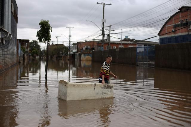 (FILES) Sander Diego uses a damaged refrigerator as a boat to carry groceries on a flooded street in Porto Alegre, Rio Grande do Sul, Brazil on May 26, 2024. Brazilian prosecutors on Friday filed an unprecedented lawsuit against oil giant Shell's subsidiary in the country, demanding $108 million in compensation over deadly 2024 floods. (Photo by Anselmo Cunha / AFP)