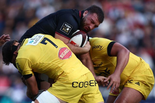 Lyon's Georgian number eight Beka Shvangiradze (C) is tackled by La Rochelle's French flanker Oscar Jégou (L) and La Rochelle's French prop Alexandre Kaddouri (R)   during the French Top 14 rugby union match between LOU Rugby and Stade Rochelais (La Rochelle) at the Gerland Stadium in Lyon, on October 10, 2026. (Photo by Alex MARTIN / AFP)