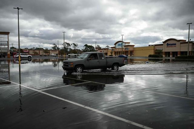 A man drives a truck through a flooded parking lot in Tiger Point, Florida, on October 10, 2026. The southeastern United States faced a high risk of flooding on Saturday as Isaias, weakened from a hurricane to a post-tropical cyclone, advanced northward from its landfall on Florida's Gulf Coast. (Photo by RONALDO SCHEMIDT / AFP)