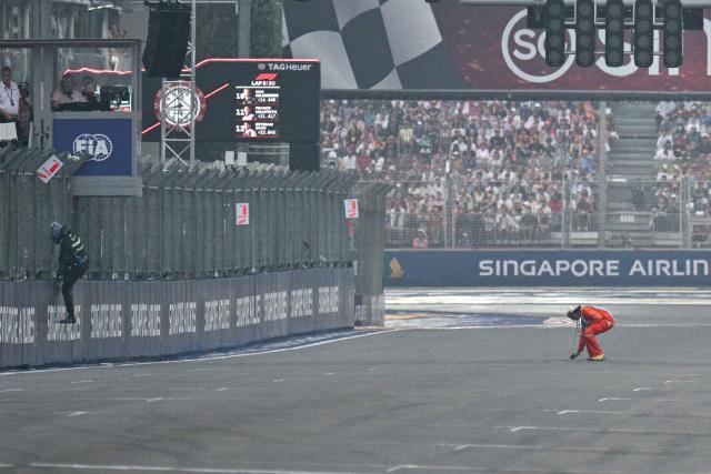 Mercedes' British driver George Russell (L) climbs through the fence after crashing as  marshal clears the debris during the sprint race ahead of the Formula One Singapore Grand Prix at the Marina Bay Street Circuit in Singapore on October 10, 2026. (Photo by ANTHONY WALLACE / AFP)