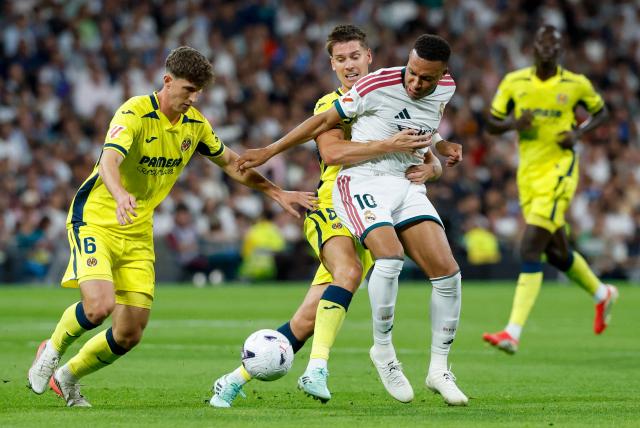 Real Madrid's French forward #10 Kylian Mbappe (C) is challenged by Villarreal's Spanish defender #06 Pau Navarro (L) and Villarreal's Argentine defender #08 Juan Foyth during the Spanish league football match between Real Madrid CF and Villarreal CF at the Santiago Bernabeu Stadium in Madrid on October 10, 2026. (Photo by Oscar DEL POZO / AFP)