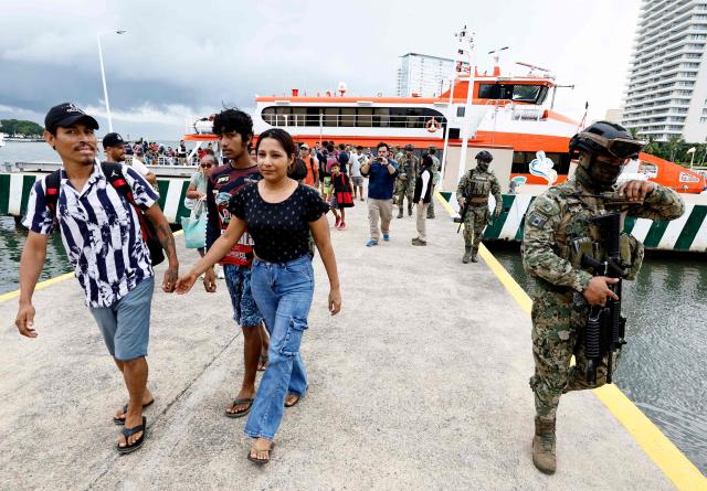 A couple walks past a Mexican Navy officer after disembarking from a ferry carrying evacuees to the 12th Naval Zone facilities in Puerto Vallarta, Jalisco state, Mexico, on October 10, 2026, ahead of the potential impact of Hurricane Simon. Hurricane Simon strengthened into a powerful Category 4 storm as it moved toward Mexico's west coast, where it was expected to make landfall late on October 10 or early on October 11. (Photo by ULISES RUIZ / AFP)
