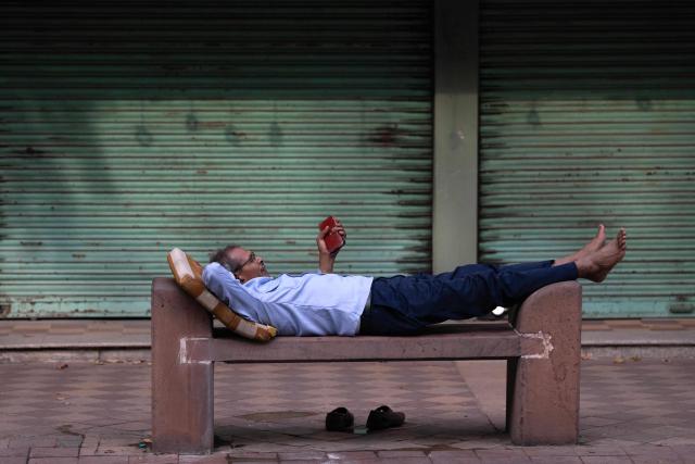 A security guard rests on a bench in front of closed shops amid ongoing protests demanding the resignation of India's Chief Election Commissioner Gyanesh Kumar over alleged voter roll irregularities linked to the "special intensive revision" (SIR), near Jantar Mantar in New Delhi on October 11, 2026. (Photo by Sajjad HUSSAIN / AFP)