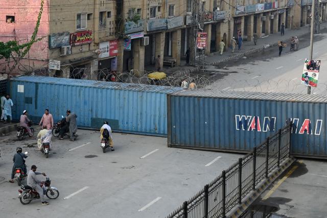 Commuters gather at a road blocked with shipping containers amid ongoing protests by the opposition Pakistan Tehreek-e-Insaf (PTI) party demanding the release of jailed former prime minister Imran Khan in Peshawar on October 11, 2026. (Photo by Abdul MAJEED / AFP)