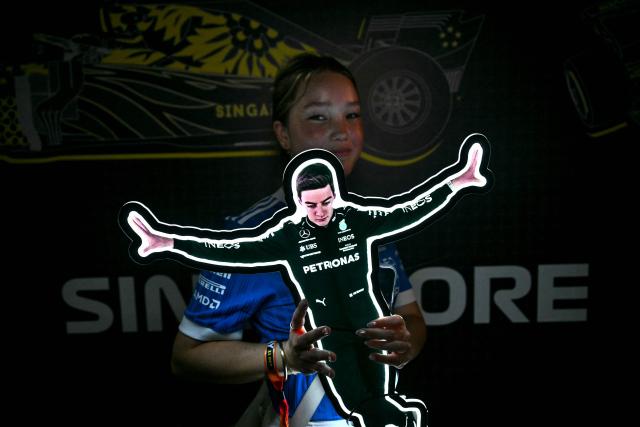 A fan poses with a cut-out of Mercedes' British driver George Russell as she heads to the stands before the start of the Formula One Singapore Grand Prix at the Marina Bay Street Circuit in Singapore on October 11, 2026. (Photo by Lillian SUWANRUMPHA / AFP)