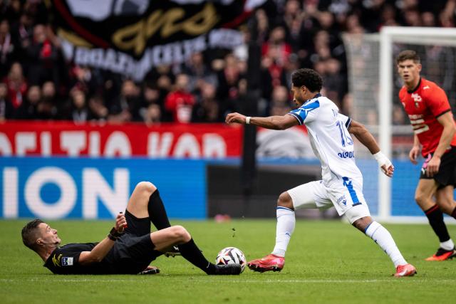 French referee Willy Delajod (L) lies on the ground as Auxerre's Cameroonian forward #10 Danny Namaso (R) dribbles the ball past him during the French L1 football match between Stade Rennais FC and AJ Auxerre at the Roazhon Park Stadium in Rennes, western France on October 11, 2026. (Photo by Guillaume SALIGOT / AFP)