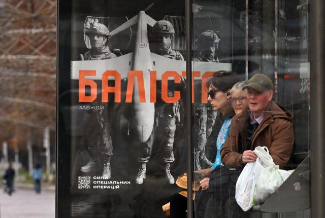 People wait for a bus at a bus stop with a recruitment placard for "Ballista", Ukraine's Forces Special Operation, in Kyiv on October 11, 2026, amid the Russian invasion of Ukraine. (Photo by Sergei SUPINSKY / AFP)