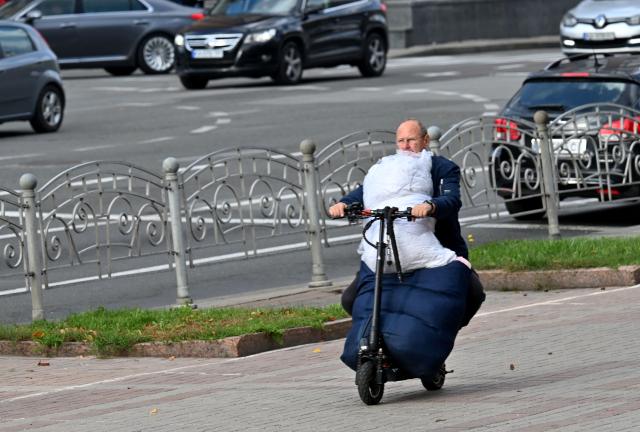A man carries his belongins as rides by electro scooter in Kyiv on October 11, 2026, amid Russian invasion in Ukraine. (Photo by Sergei SUPINSKY / AFP)