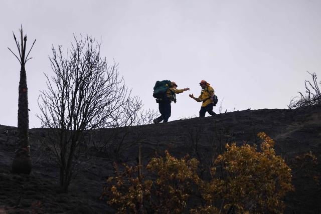 Firefighters greet each other atop a ridge while fighting the Bike fire in the outskirts of Santa Clarita, California on October 11, 2026. Los Angeles County Fire is battling a fast moving wildfire that started on Sunday afternoon threatening homes in Santa Clarita, the third largest city in Los Angeles County. The LA County Sheriff's office ordered residents to evacuate as the Bike fire grew to 100 acres in size in a very short time. (Photo by David Swanson / AFP)