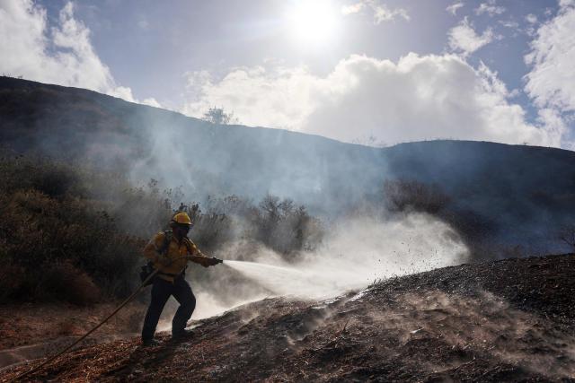 A firefighter sprays a hotspot while fighting the Bike fire in the outskirts of Santa Clarita, California on October 11, 2026. Los Angeles County Fire is battling a fast moving wildfire that started on Sunday afternoon threatening homes in Santa Clarita, the third largest city in Los Angeles County. The LA County Sheriff's office ordered residents to evacuate as the Bike fire grew to 100 acres in size in a very short time. (Photo by David Swanson / AFP)