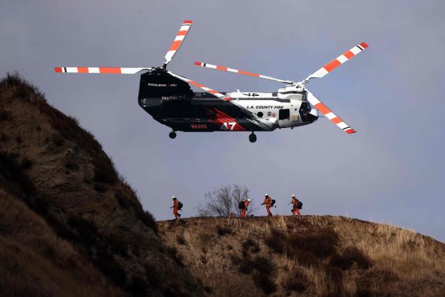 An LA County Fire helicopter flies above crews fighting the Bike fire in the outskirts of Santa Clarita, California on October 11, 2026. Los Angeles County Fire is battling a fast moving wildfire that started on Sunday afternoon threatening homes in Santa Clarita, the third largest city in Los Angeles County. The LA County Sheriff's office ordered residents to evacuate as the Bike fire grew to 100 acres in size in a very short time. (Photo by David Swanson / AFP)