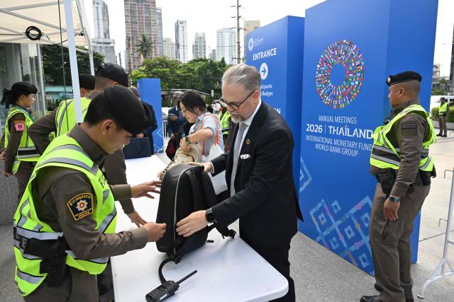People pass through a security checkpoint outside Queen Sirikit National Convention Center on the opening day of the annual meetings of the International Monetary Fund and the World Bank in Bangkok on October 12, 2026. Finance ministers and central bankers meet in Bangkok this week for the annual gatherings of the International Monetary Fund and World Bank, with the global economy buffeted between the US-Iran war's energy shock, rising debt pressures and the AI boom. (Photo by Panumas Sanguanwong / AFP)