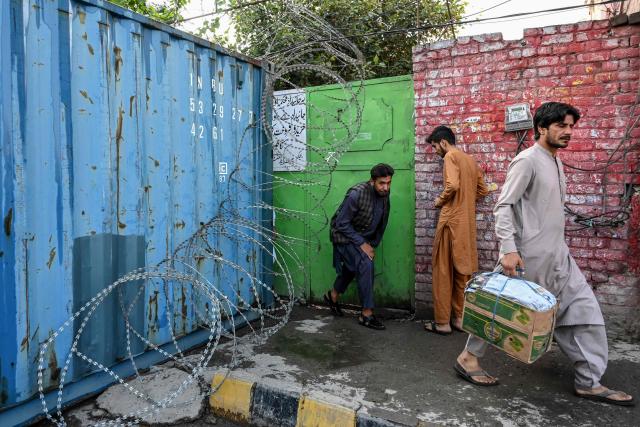 People walk next to a shipping container along a blocked road after the imposition of an emergency rule in Peshawar on October 12, 2026 following anti-government demonstrations by the opposition Pakistan Tehreek-e-Insaf (PTI) party demanding the release of jailed former prime minister Imran Khan. Pakistan placed a northern province under emergency rule on October 11, the president's office said, following anti-government demonstrations by supporters of jailed former prime minister Imran Khan and militant violence in the northwest. (Photo by Abdul MAJEED / AFP)