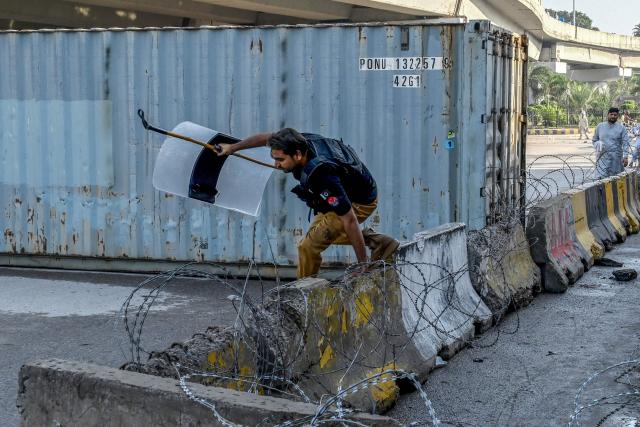 A policeman jumps over a barricade along a blocked road after the imposition of an emergency rule in Peshawar on October 12, 2026 following anti-government demonstrations by the opposition Pakistan Tehreek-e-Insaf (PTI) party demanding the release of jailed former prime minister Imran Khan. Pakistan placed a northern province under emergency rule on October 11, the president's office said, following anti-government demonstrations by supporters of jailed former prime minister Imran Khan and militant violence in the northwest. (Photo by Abdul MAJEED / AFP)