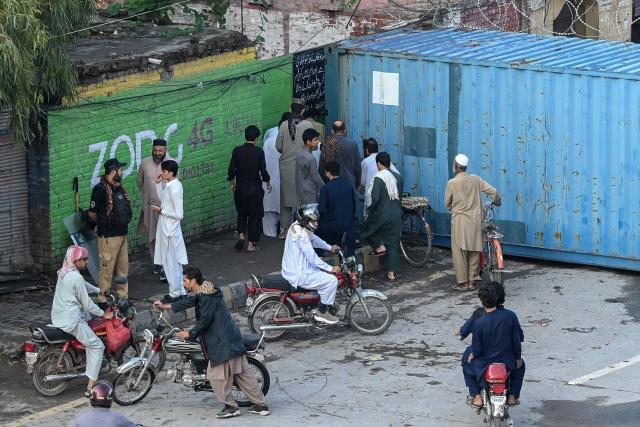 People walk through a gap between a wall and a shipping container at a blocked road after the imposition of an emergency rule in Peshawar on October 12, 2026 following anti-government demonstrations by the opposition Pakistan Tehreek-e-Insaf (PTI) party demanding the release of jailed former prime minister Imran Khan. Pakistan placed a northern province under emergency rule on October 11, the president's office said, following anti-government demonstrations by supporters of jailed former prime minister Imran Khan and militant violence in the northwest. (Photo by Abdul MAJEED / AFP)