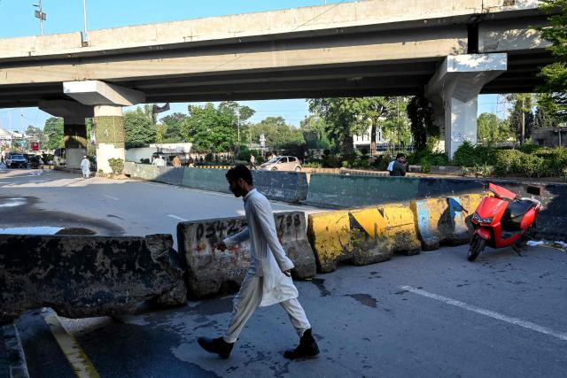 A man walks past barricades along a blocked road after the imposition of an emergency rule in Peshawar on October 12, 2026 following anti-government demonstrations by the opposition Pakistan Tehreek-e-Insaf (PTI) party demanding the release of jailed former prime minister Imran Khan. Pakistan placed a northern province under emergency rule on October 11, the president's office said, following anti-government demonstrations by supporters of jailed former prime minister Imran Khan and militant violence in the northwest. (Photo by Abdul MAJEED / AFP)
