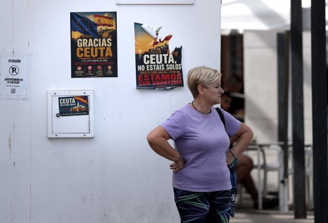 A person stands next to posters thanking the inhabitants of Ceuta for protesting against the migration crisis coming from Morocco and reading 'Ceuta, you are not alone' in Spain's north African enclave of Ceuta on October 11, 2026. Spain's King Felipe VI and Queen Letizia are scheduled to visit Ceuta on October 13, 2026. The Spanish North African enclave of some 80,000 inhabitants seek to regain balance while hundreds of migrants remain in makeshifts camp after the massive influx of tens of thousands of migrants from Morocco in late July. (Photo by Thomas COEX / AFP)