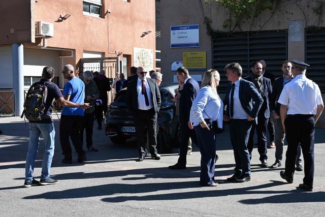 People stand in front of Joseph-Lakanal high school after a headmaster was shot and wounded with a hunting rifle and a teenager was arrested in Aubagne, southern France, on October 12, 2026. The prime minister's office said the principal's life was not in danger and that the interior and education ministers were heading to the scene. (Photo by Miguel MEDINA / AFP)