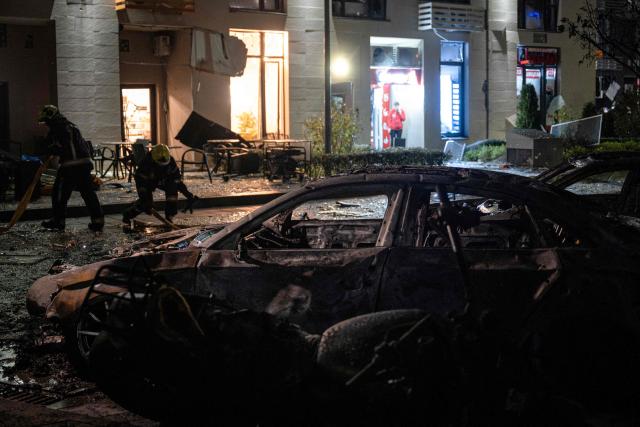 Ukrainian firefighters work by wreckage cars in front of a high-rise residential building damaged following a Russian drone attack, in Kyiv on October 12, 2026, amid the Russian invasion of Ukraine. (Photo by Genya SAVILOV / AFP)
