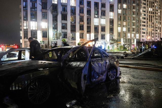 Ukrainian firefighters inspect burned vehicles in front of a high-rise residential building damaged following a Russian drone attack, in Kyiv on October 12, 2026, amid the Russian invasion of Ukraine. (Photo by Genya SAVILOV / AFP)