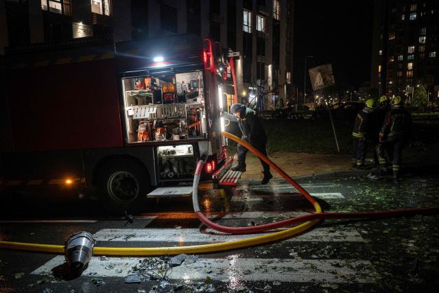 A fragment of a drone lies on the road next to Ukrainian firefighters working near a high-rise residential building damaged following a Russian drone attack, in Kyiv on October 12, 2026, amid the Russian invasion of Ukraine. (Photo by Genya SAVILOV / AFP)